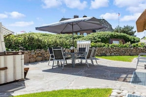 An outdoor patio with a stone table and chairs, a large umbrella, and a stone wall. - Holiday home in Rantum with swimming pool (Rantum)