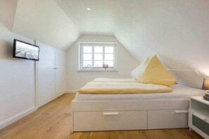 A bedroom with a sloped ceiling, a bed with white bedding, a window with white frames, and a flat-screen TV mounted on the wall. - Holiday home in Rantum with swimming pool (Rantum)