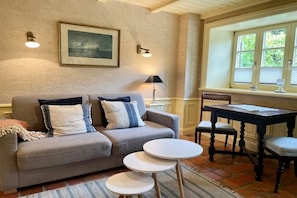 A cozy living room with a sofa, two side tables, a wooden chair, and a window with blinds. - Holiday apartment in Sylt with 1 bedroom (Sylt \/ Alt Westerland)