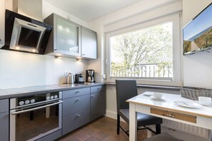 A compact kitchen with a built-in oven, a coffee maker, and a window with a view of trees. - Holiday home in Sylt with swimming pool (Sylt)