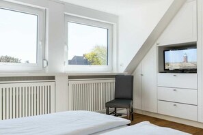 Un dormitori amb un llit, una cadira, una televisió i una finestra amb vista a un edifici.