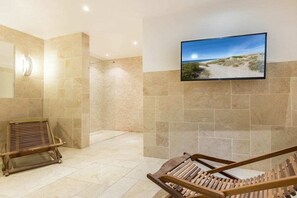 A modern interior with a large flat-screen TV mounted on a wall, a wooden bench, and a tiled floor. - Holiday apartment in Sylt with 2 bedrooms (Sylt Westerland)