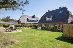 A residential property with a well-maintained lawn, a wooden deck, and a stone wall. - Holiday apartment in Sylt with 3 bedrooms (Sylt Westerland)