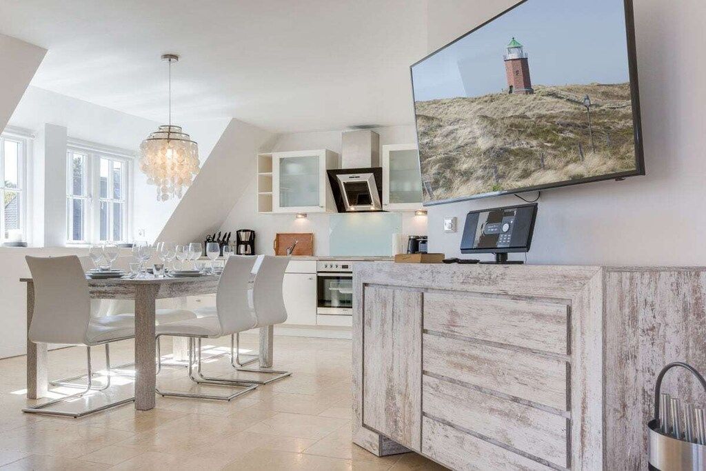 A modern kitchen with a dining area, a large TV mounted on the wall, and a view of a lighthouse.