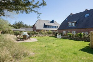 A residential property with a well-maintained lawn, a patio with outdoor furniture, and a brick house with multiple windows and a sloped roof. - Holiday apartment in Sylt with 3 bedrooms (Sylt Westerland)