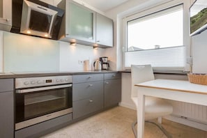 A modern kitchen with a built-in oven, a coffee maker, and a window with blinds. - MeerZeit - Süderstraße (Sylt)