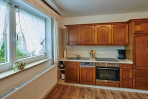 Een keuken met houten kastjes, een inbouwoven, een spoelbak en een raam met gordijnen.