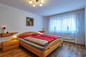 A bedroom with a wooden bed, bedside tables, a nightstand, a painting on the wall, and a window with curtains. - Holiday apartment with 2 bedrooms (Strullendorf)