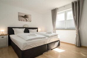 A modern bedroom with a large bed, bedside lamps, a window with curtains, and a wall-mounted artwork. - One Putt Ground Floor (Göhren-Lebbin)