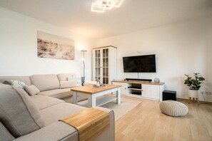 A modern living room with a sofa, coffee table, TV, cabinet, and decorative plants. - One Putt Ground Floor (Göhren-Lebbin)