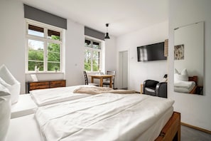 A bedroom with two beds, a desk, a chair, a TV, and a large window. - Roggenkammer Double Room with Garden View – Hotel Bolter Mühle on Lake Müritz (Rechlin)