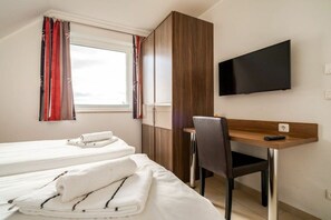 Habitació d'hotel amb dos llits, un escriptori amb una cadira, un televisor fixat a la paret i una finestra amb cortines.