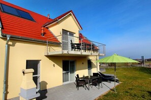 Een gebouw met twee verdiepingen, een rood dak, een balkon en een patio met tuinmeubilair.