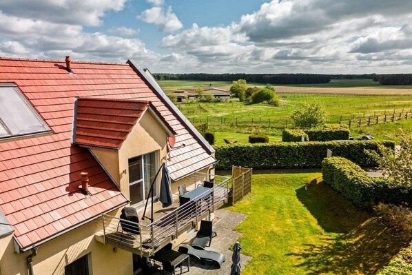 A house with a sloped roof, a balcony, and a view of a green field. - Lontargos upper floor apartment (Göhren-Lebbin)