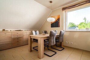 A dining area with a wooden table and chairs, a pendant light, and a window with curtains. - Lontargos upper floor apartment (Göhren-Lebbin)