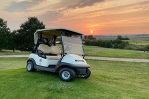 Een golfkarretje geparkeerd op een grasveld, met een zonsondergang op de achtergrond.