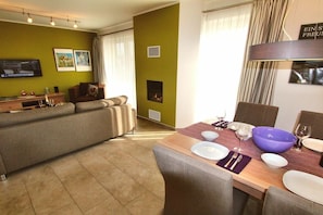 A modern living room with a sofa, a dining table set for four, and a fireplace. - HOUSE TRAKEHNEN / GROUND FLOOR APARTMENT (Göhren-Lebbin)