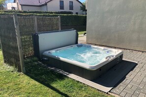Ett bubbelbad utomhus, omgivet av ett trästaket och en stenlagd yta.
