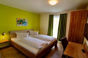 A hotel room with two beds, a wooden table, a chair, a painting on the wall, and a window with curtains. - HOUSE TRAKEHNEN / GROUND FLOOR APARTMENT (Göhren-Lebbin)
