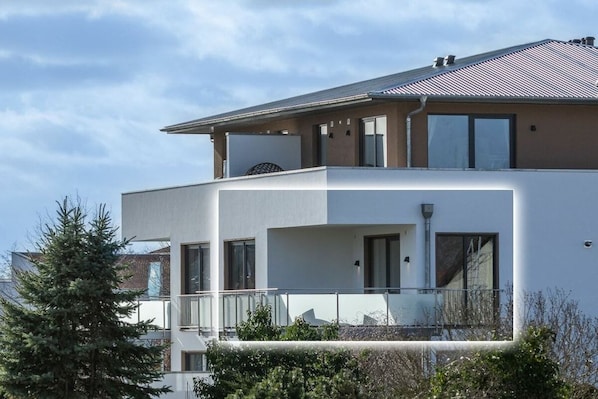 Un edificio residencial moderno de dos pisos, con balcón, ventanas amplias y techo plano.