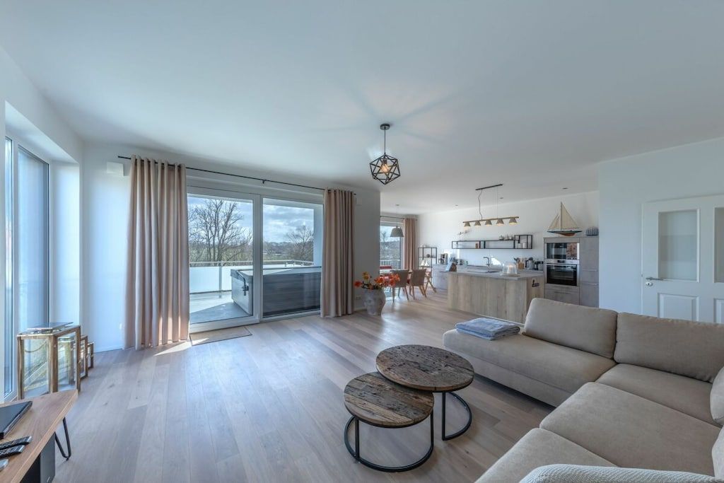 A modern living room with a sofa, two round tables, and a view of the kitchen and balcony.