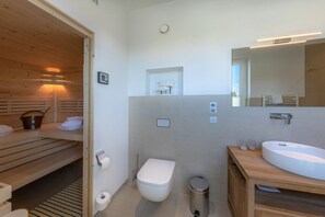 Moderni kylpyhuone, jossa on puinen sauna, wc, pesuallas ja peili.