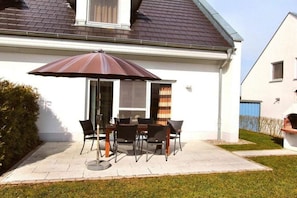 A patio with a table and chairs, a large umbrella, and a house with a sloped roof. - Holiday Home Morning Sun (Göhren-Lebbin)