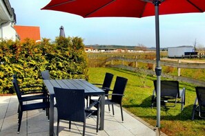 Eine Terrasse im Freien mit Tisch und Stühlen, einem roten Sonnenschirm und Blick auf eine Brücke sowie Gebäude in der Ferne.