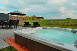 An outdoor hot tub area with lounge chairs and a table, surrounded by a stone wall and a grassy field. - Luxury holiday home Limerick (Göhren-Lebbin)