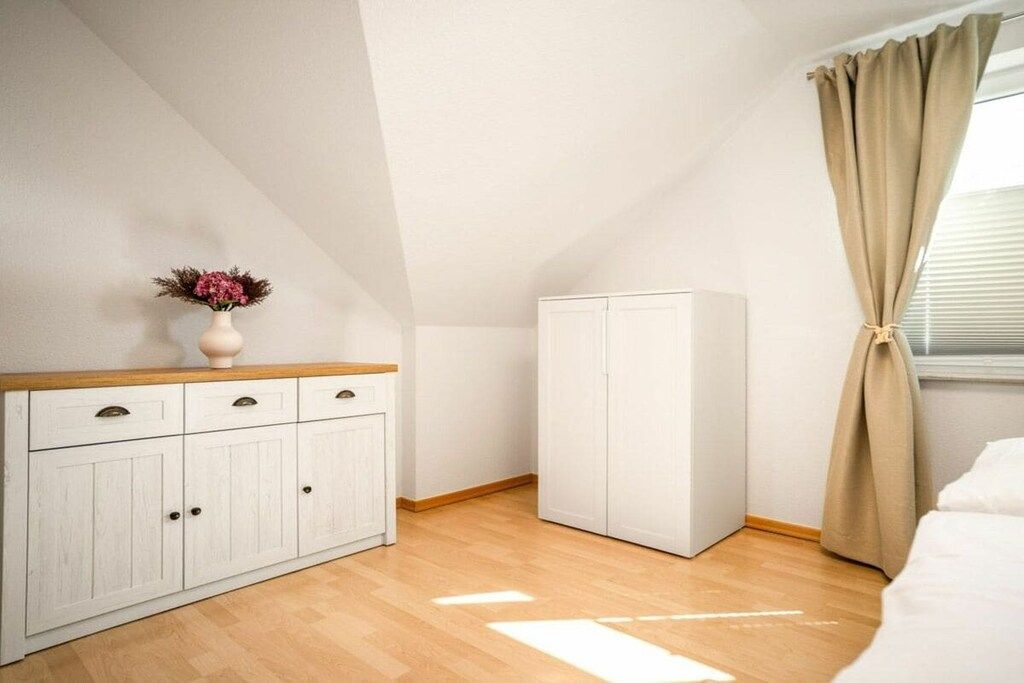 Une chambre à coucher avec une commode en bois, une armoire et une fenêtre avec des rideaux.