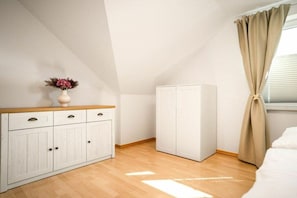 Une chambre à coucher avec une commode en bois, une armoire et une fenêtre avec des rideaux.