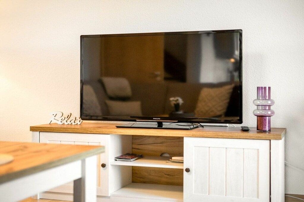 Un téléviseur à écran plat posé sur un meuble télé en bois, avec une étagère en dessous.