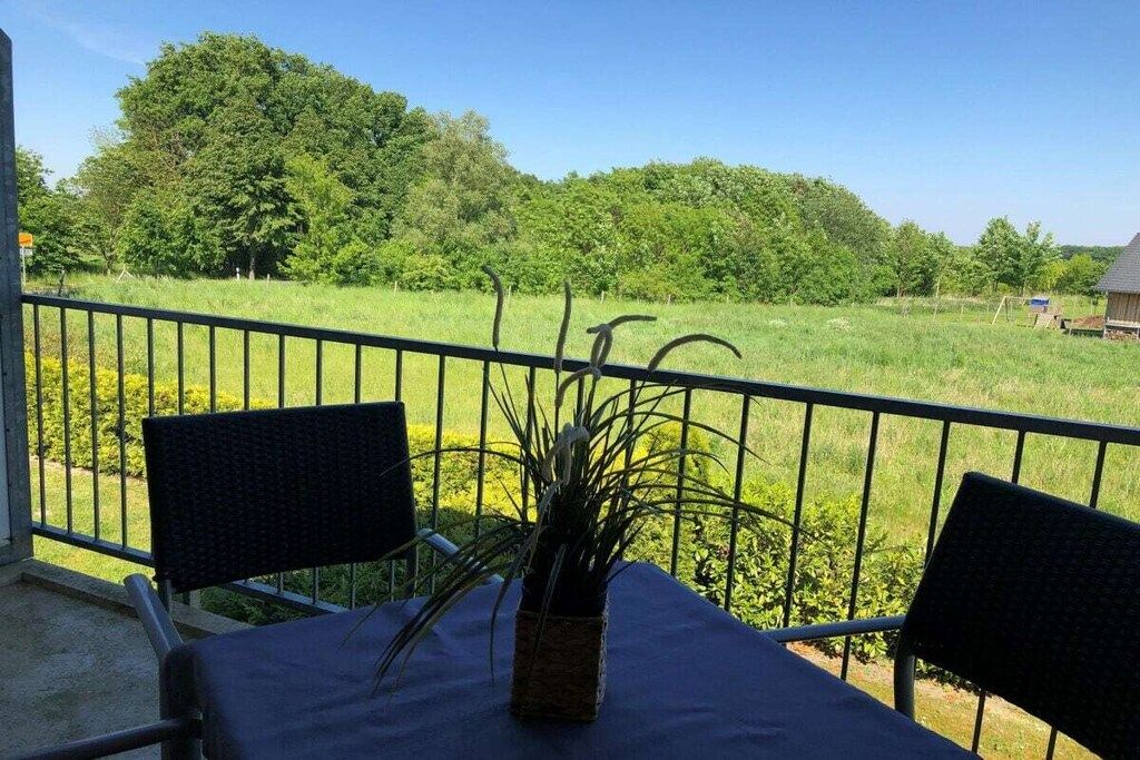 A balcony with two chairs and a table, overlooking a grassy area with trees.