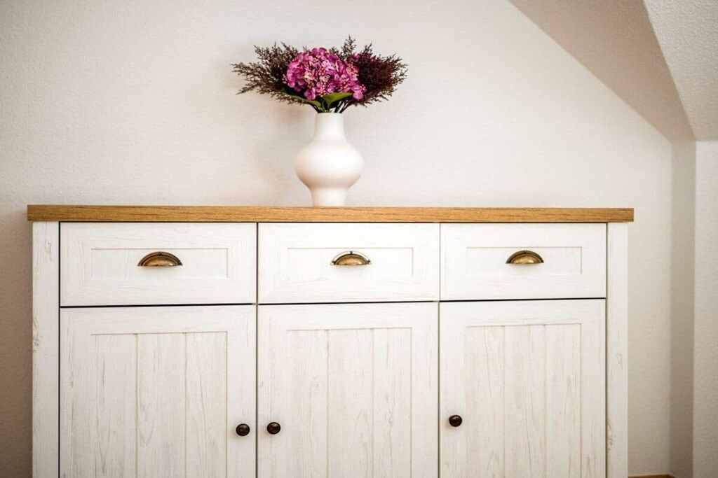 Een wit houten kastje met drie lades en twee deuren, met een houten plank aan de bovenkant.