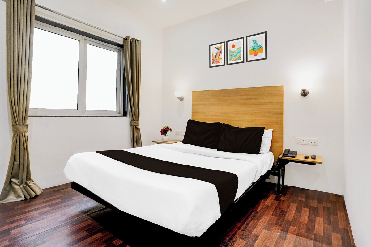 Una habitación de hotel con cama, mesita de noche, ventana con cortinas y una obra de arte en la pared.