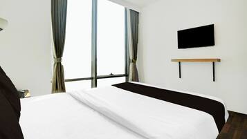 Una habitación de hotel con una cama grande, un televisor de pantalla plana en la pared y una ventana con cortinas.