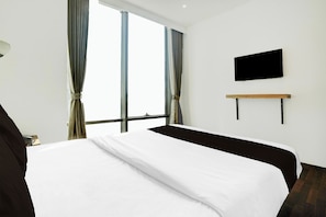 Una habitación de hotel con una cama grande, un televisor de pantalla plana en la pared y una ventana con cortinas.