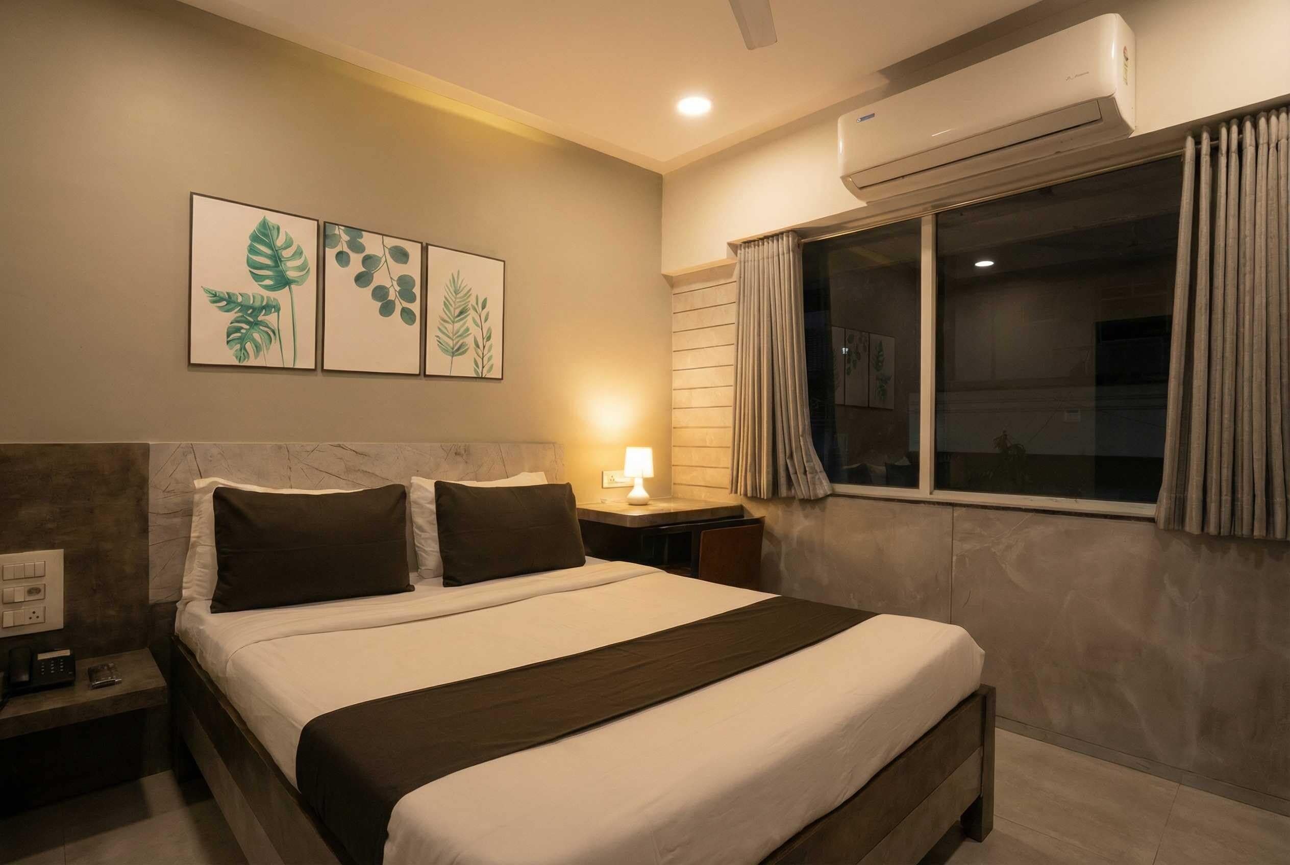 Un dormitorio con cama, mesitas de noche, aire acondicionado instalado en la pared y una ventana con cortinas.