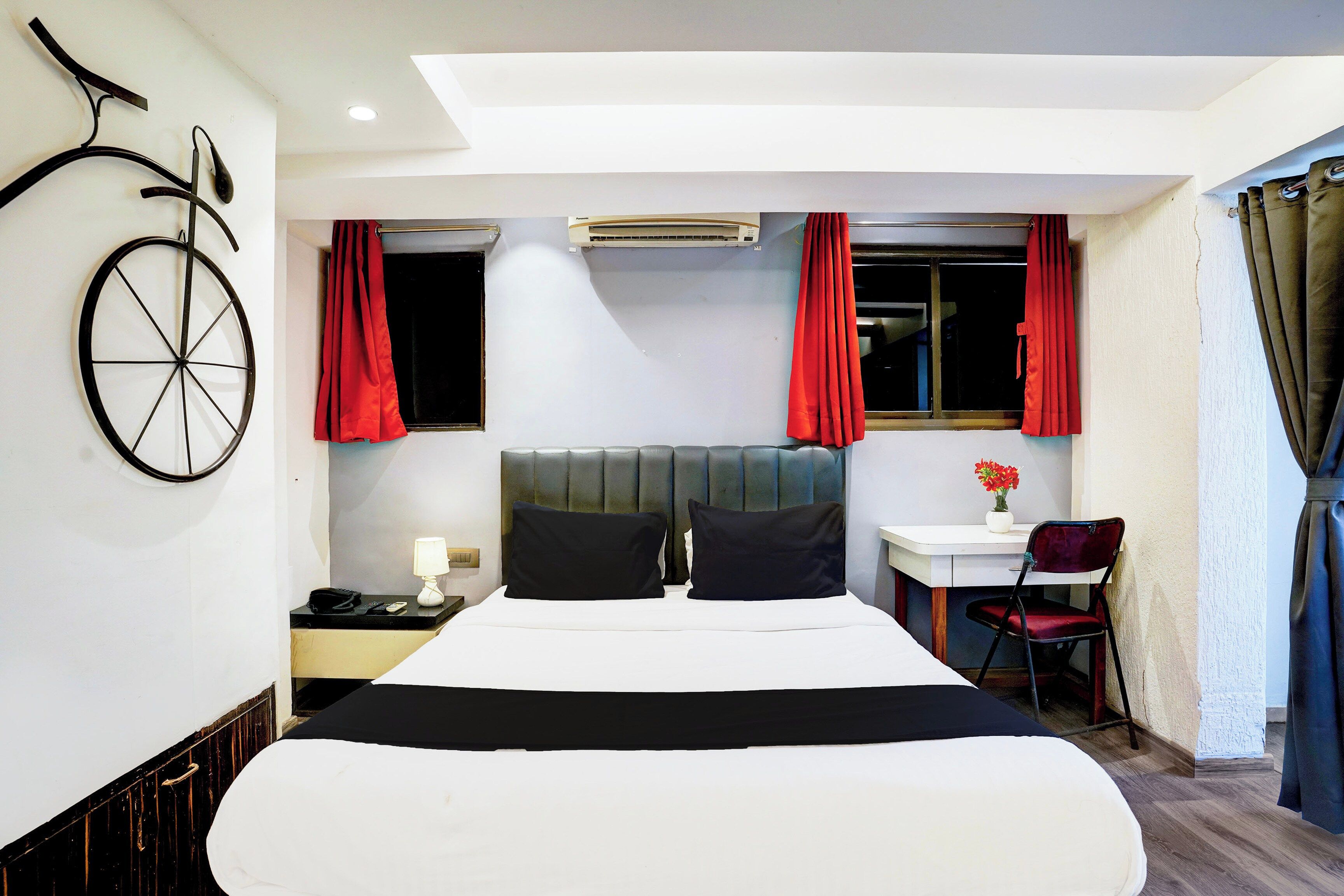 A hotel room with a bed, a desk, a chair, a telephone, and an air conditioning unit.