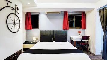 A hotel room with a bed, a desk, a chair, a telephone, and an air conditioning unit.