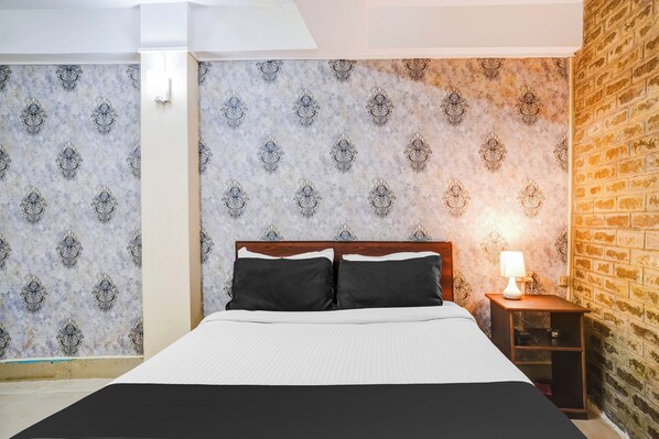 A bedroom with a bed, a nightstand, a lamp, and a brick wall.