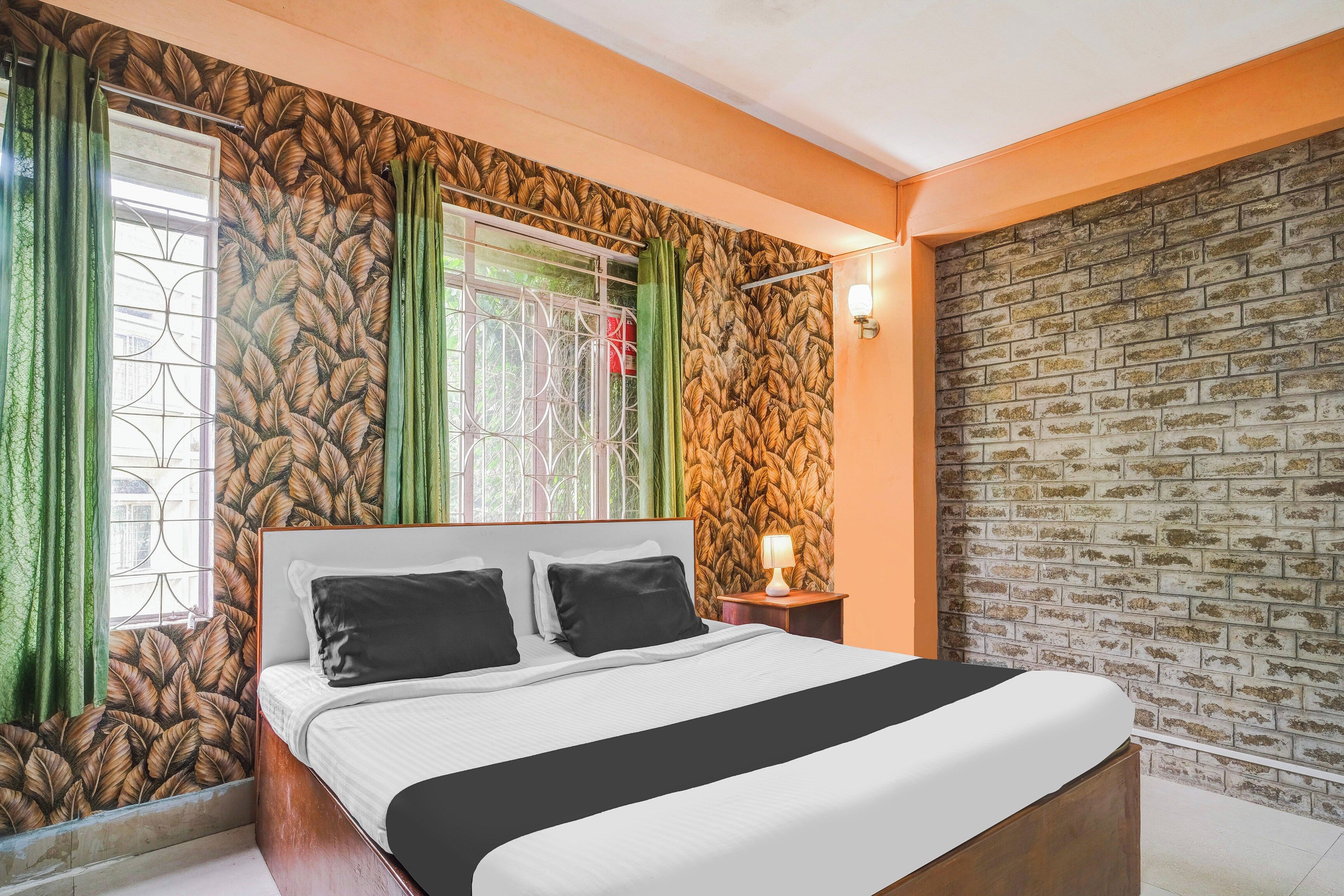 Un dormitorio con cama, ventana con cortinas, pared con diseño de hojas y pared de ladrillo.