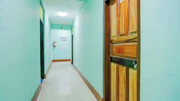 Un couloir avec une porte en bois sur la droite, un extincteur sur la gauche et un panneau indiquant la direction à suivre pour rejoindre la maison d’hôtes Balaji.
