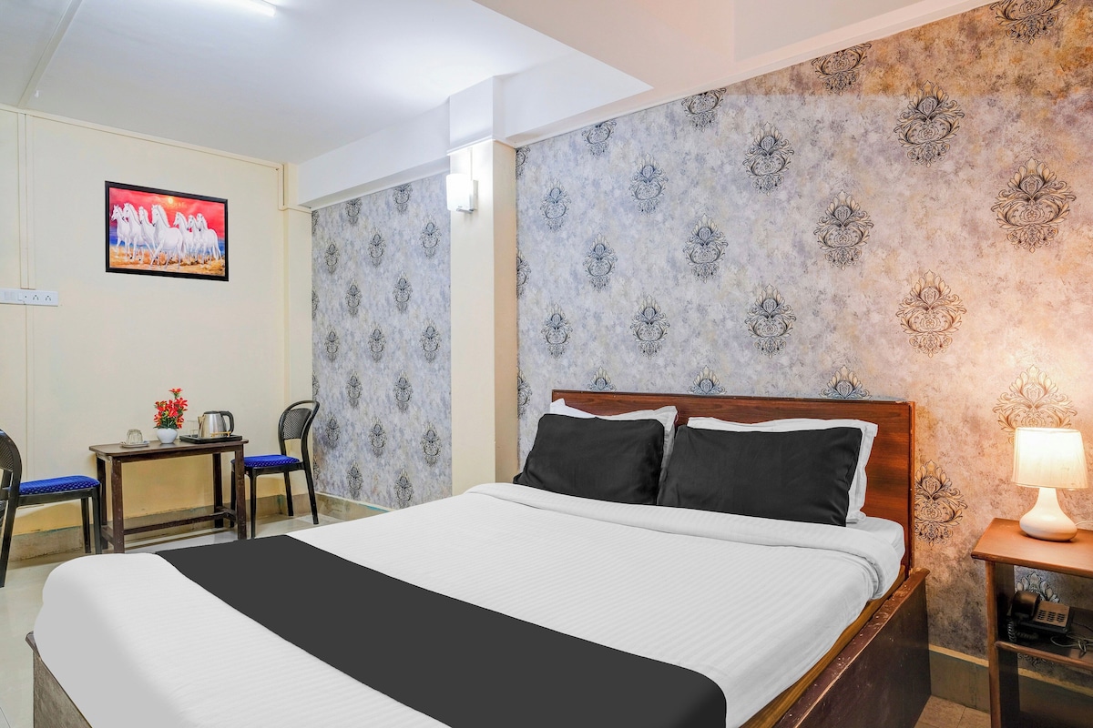 A hotel room with a bed, a desk with a chair, a TV on the wall, and patterned wallpaper.