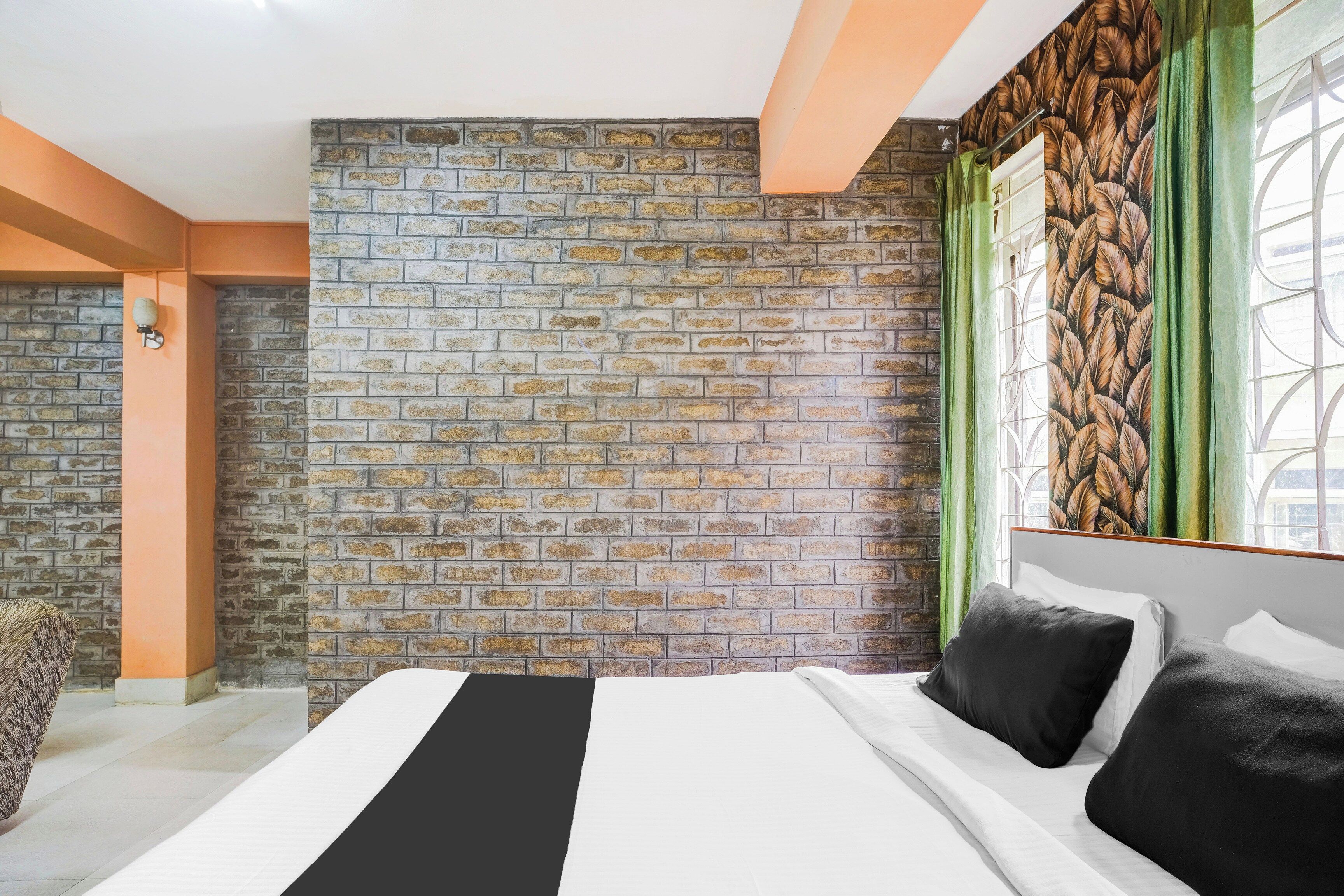 Une chambre avec un mur en briques, un lit avec une literie blanche et noire, et une fenêtre avec des rideaux verts.