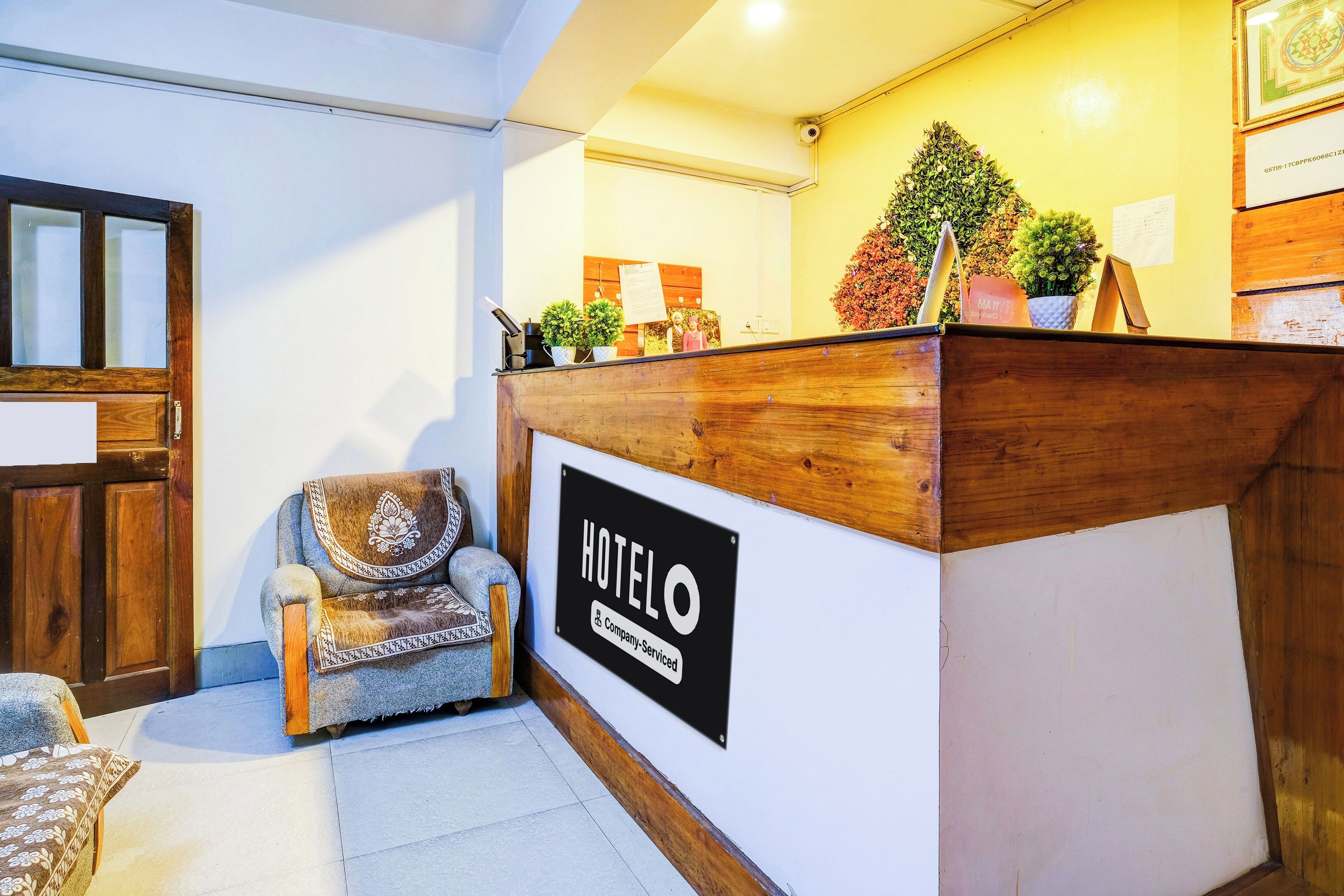 Un mostrador de recepción de hotel con un cartel que indica que es un servicio de empresa. Hay un mostrador de madera, una silla con cojín y una pequeña planta en maceta sobre el mostrador.