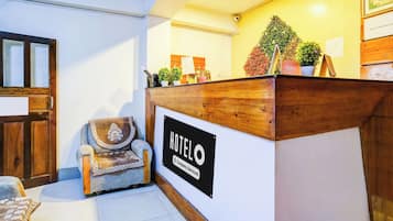 Un mostrador de recepción de hotel con un cartel que indica que es un servicio de empresa. Hay un mostrador de madera, una silla con cojín y una pequeña planta en maceta sobre el mostrador.