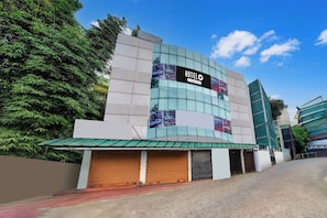 Un edificio moderno con un amplio frente de vidrio, un cartel que dice 'HOTELO' en el lateral y una entrada con portones.