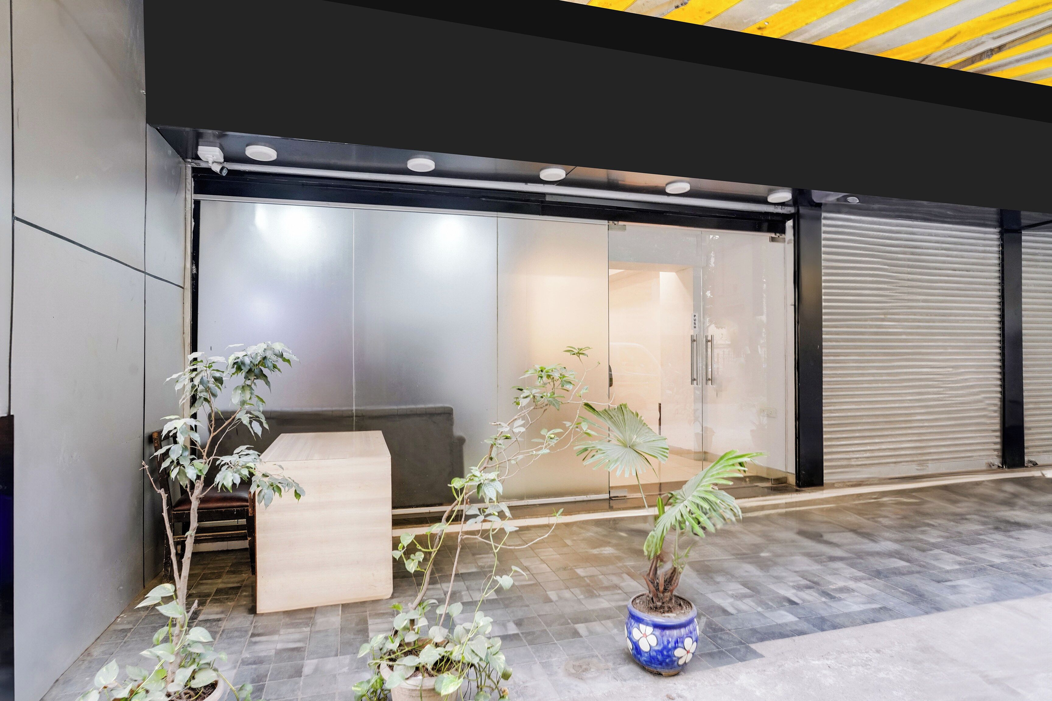 A modern building entrance with a reception desk, a glass door, and potted plants.