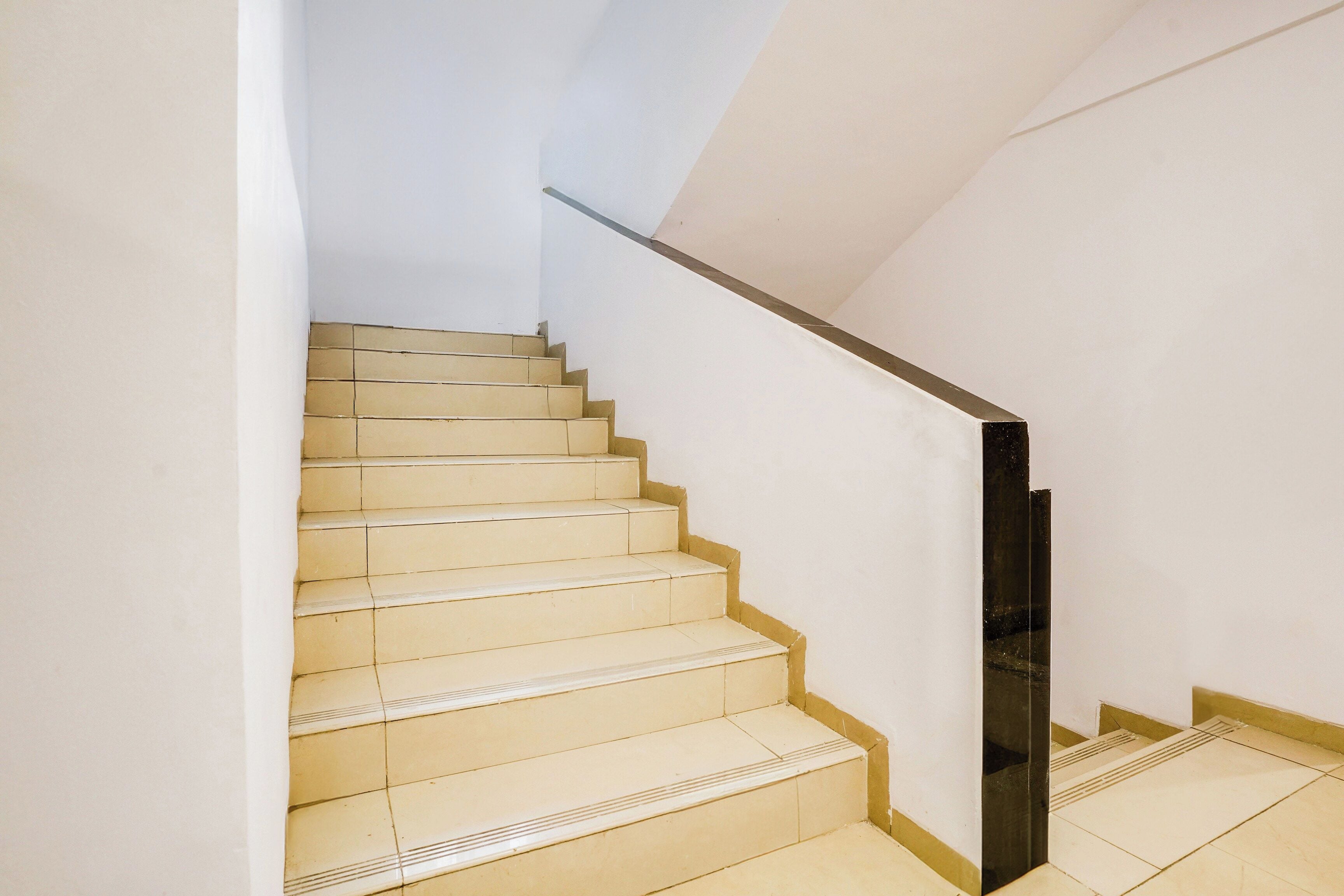 A staircase with beige steps and a black handrail, leading to a landing.
